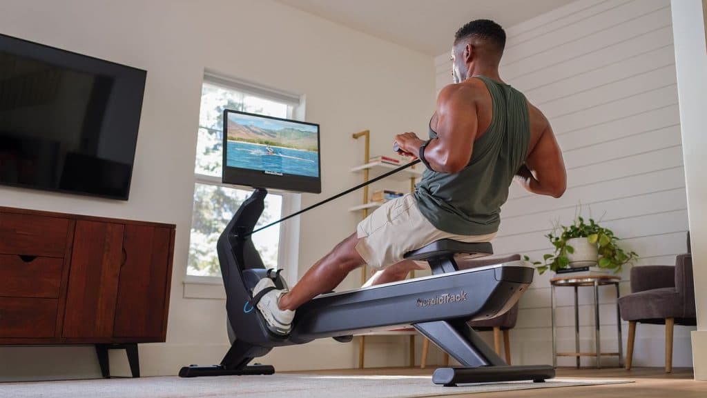Individual using a NordicTrack RW900 rower at home with an iFIT scenic rowing workout displayed on the touchscreen.